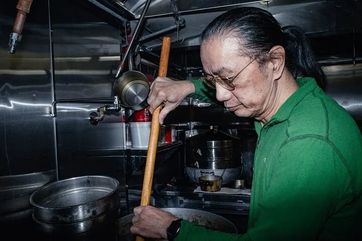 A cook stirring a pot of congee in the kitchen