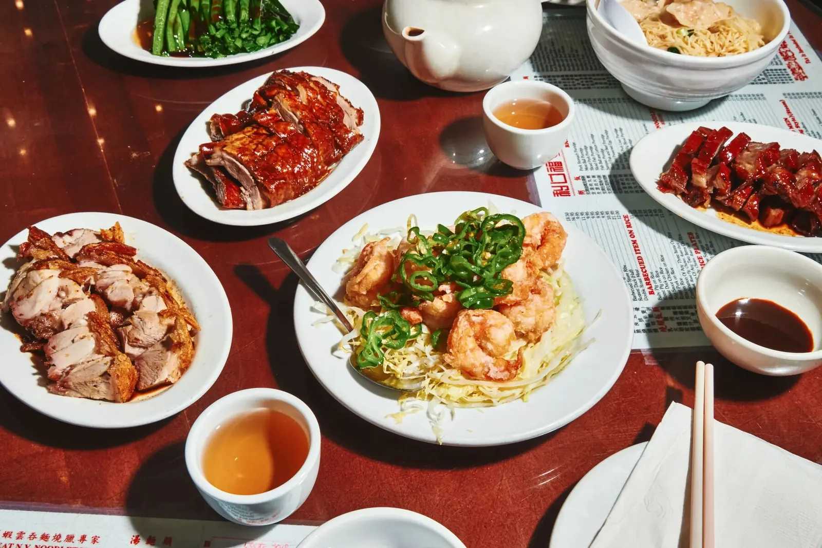 Roast duck, char siu, roast pork and fried shrimp on the table with a paper menu placemat